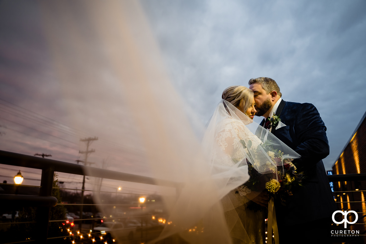 Groom kissing his bride as her veil blows into the wind.